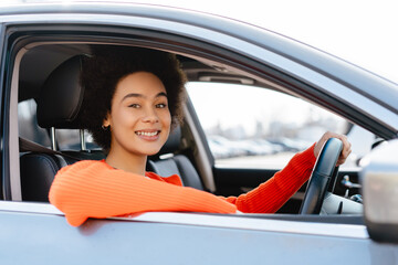 Attractive, smiling African American woman driving car, looking at camera. Concept of transportation