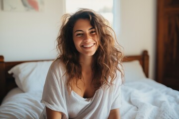 Beautiful young woman smiling sitting on bed in front of her laptop In the bright morning