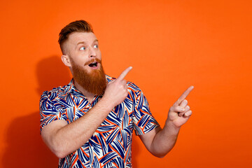 Photo of excited cheerful guy dressed print shirt looking pointing two fingers emtpy space isolated orange color background