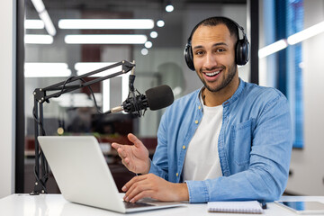 Portrait of a smiling young Muslim man sitting in headphones in the office at the table, talking...
