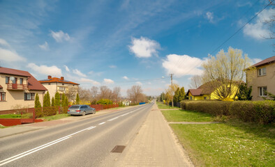 Wiosna na wzgórzach koło Ostrowca (Szewna) pod błękitnym niebem. Droga biegnąca przez sąsiednią miejscowość tuż przed Ostrowcem. Piękne niebo z delikatnymi chmurami. - obrazy, fototapety, plakaty