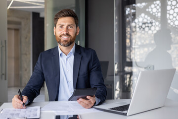 Portrait of a young male accountant, insurance expert, analyst working in the office with documents and a calculator, smiling and looking at the camera