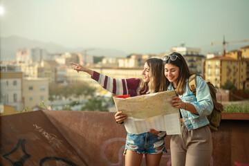 Two Caucasian girls in casual clothes sightseeing and looking at a map in Malaga, Spain.