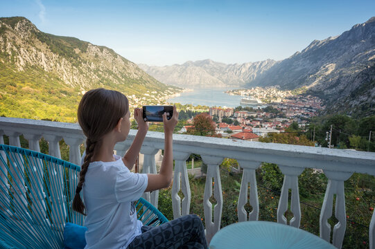 Rear view of little girl take pictures with her smartphone from the terrace of a room with an amazing panoramic view of the picturesque Bay of Kotor in Montenegro