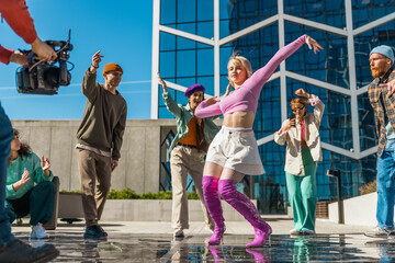 Behind The Scenes: Outdoor Scene Captures A Group Of Young Adults Joyfully Dancing In A City Plaza, Showcasing A Blend Of Fashion And Dynamic Movement. Operator Filming Dancers On Professional Camera.