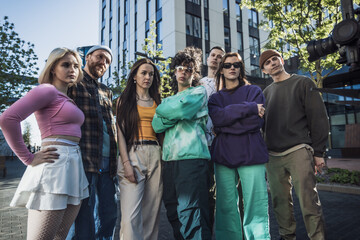 Group Of Young Adults In Eclectic Outfits Poses Confidently In An Urban Setting, Showcasing A Mix...
