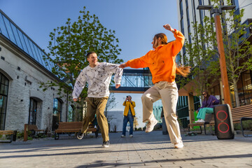Vibrant Outdoor Scene Capturing Two Young Adults Joyfully Dancing In A Sunny Urban Plaza,...