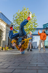 Vertical Screen: Young And Athletic B-Boy Breakdancing To Break Beats Downtown On City Street Among Modern Buildings In The Circle Of Friends. Stylish Young People Supporting Professional Dancer.
