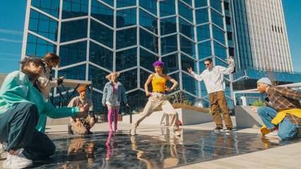 Vibrant Outdoor Scene Of Diverse Young Adults Energetically Dancing In Front Of A Modern Glass Building, Showcasing Friendship And Cultural Expression Through Dynamic Movements And Casual Urban Wear.