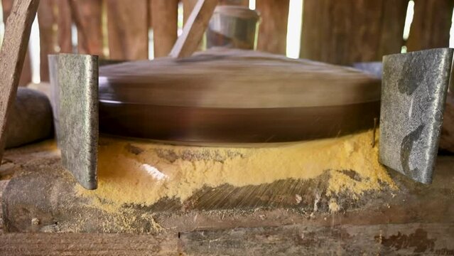 A millstone is spinning. A stone grinds grain in a mill. Production of corn flour. Corn kernels fall into the mill. Traditional watermill on the river.