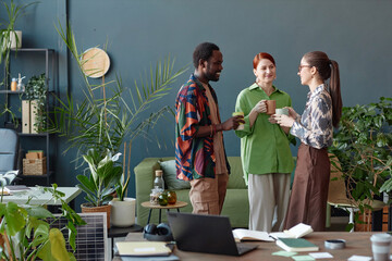 Creative business team of three people communicating standing in modern office at coffee break against blue wall copy space
