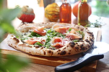 Wood fired Italian pizza with prosciutto, parma ham, arugula, and parmesan, on a wooden cutting board, selective focus.