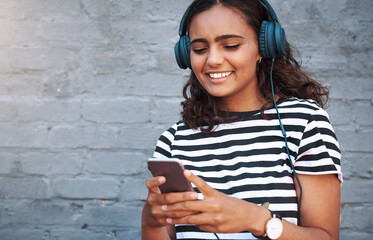 Girl, headphones and cellphone with wall background in city for music listening, subscription or...