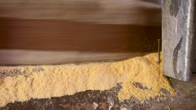 A millstone is spinning. A stone grinds grain in a mill. Production of corn flour. Corn kernels fall into the mill. Traditional watermill on the river.	