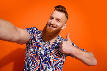 Photo of good mood confident guy dressed print shirt tacking selfie showing thumb up isolated orange color background