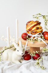 Obraz na płótnie Canvas Festive table setting with ceramic bunny, red eggs, candles and Easter pastries, vertical photo. Easter holiday concept.
