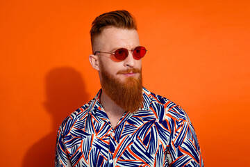Portrait of cool man with trendy haircut wear print shirt in glasses look at logo empty space isolated on vivid orange color background