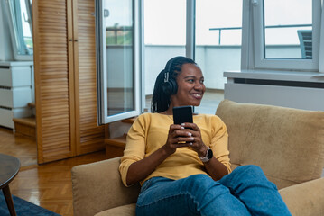 Rest And Relax Concept. Portrait of smiling African American woman using cell phone wearing wireless headset listening to music online, cheerful casual lady enjoying her playlist, free copy space