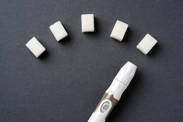Blood sugar level displayed with sugar cubes and a lancet pen on a dark background