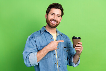 Photo of cool positive guy dressed jeans shirt pointing finger beverage empty space isolated green color background