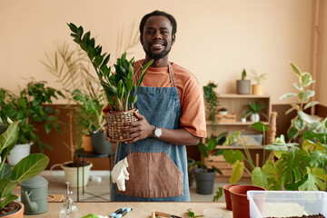 Waist up portrait of smiling African American man holding potted plant while enjoying gardening at home and looking at camera copy space 