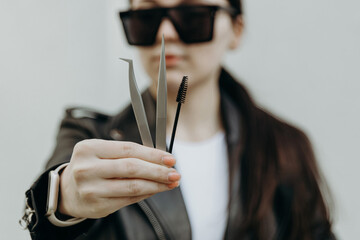 The girl shows tweezers and a brush for eyelash extensions.