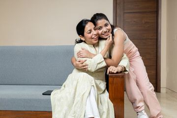 Indian Mother and Teen young daughter sitting on sofa at home looking towards the camera ,Happy Young teen hug Mother in living room having candid moments