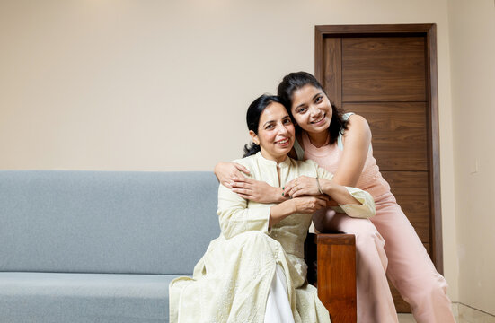 Indian Mother and Teen young daughter sitting on sofa at home looking towards the camera ,Happy Young teen hug Mother in living room