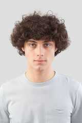 smiling and handsome a young man with curly hair he looks into the camera with his blue eyes, portrait of guy isolated against a gray background