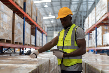 African American male warehouse worker wear safety uniform, helmet and scanning barcodes on boxes...