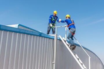 Two construction workers wearing safety gear climb up a ladder to the roof of a building