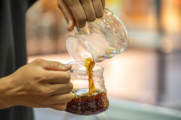 The barista carefully pours the coffee from one glass container to another.