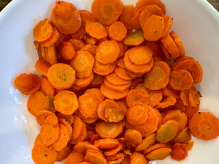Cooked, sliced, orange carrots with seasoning in a white bowl