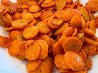 Cooked, sliced, orange carrots with seasoning in a white bowl