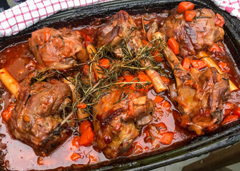 Roasted lamb shanks in a pan with sauce, carrots, and rosemary