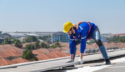 A solar panel installer wearing a safety harness and hard hat is installing solar panels on a...