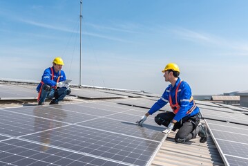 Two solar panel technicians in hardhats and safety gear inspect the installation on a commercial...