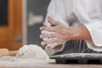 professional Chef sifting flour powder and sprinkling ingredients on massaging dough for bakery...