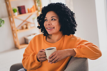 Photo portrait of lovely young lady drink coffee look empty space dressed casual orange clothes cozy day light home interior living room - obrazy, fototapety, plakaty