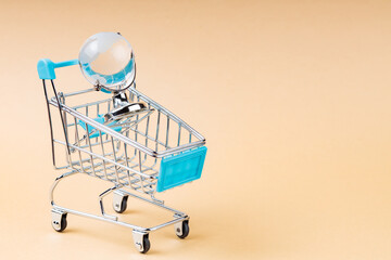 Shopping Cart with Glass Globe on Beige Background, World Trade Concept, Copy Space
