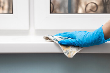housewife wearing gloves wipes a plastic window sill.