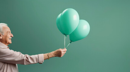 An elderly gray-haired man holds out balloons on a green background