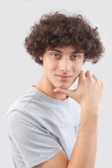 Smiling and handsome a young man with curly hair he looks into the camera with his blue eyes, his hands on his face, a portrait of a guy wearing a T-shirt isolated against a gray background