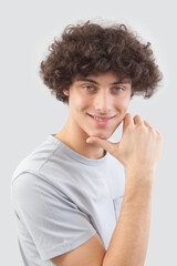 Smiling and handsome a young man with curly hair he looks into the camera with his blue eyes, his hands on his face, a portrait of a guy wearing a T-shirt isolated against a gray background