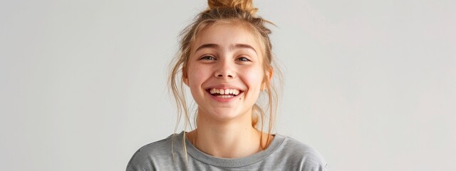 Teen Laughing in Casual Attire: Heartfelt laughter captured in a teenage girl with blond hair, casually dressed in a gray T-shirt, against a minimalist background. - obrazy, fototapety, plakaty