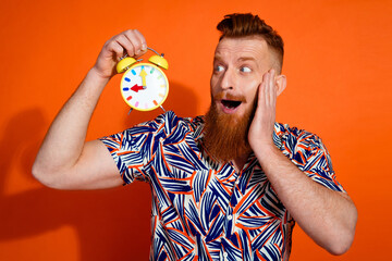 Photo of impressed funky guy dressed print shirt arm cheek looking clock isolated orange color background