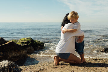 A happy mother holds her smiling son in her arms by the sea, enjoying the sea.cheerful mother and son. walk along the seashore mother and son . hugging mother and son