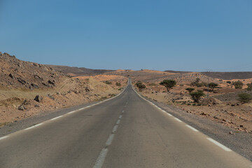 Fototapeta na wymiar A straight road leading through the sand and dunes of the Sahara Desert