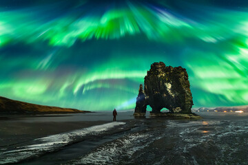 A man with a lantern (headlight) watches the  Northern Lights (Aurora Borealis) dance across the...