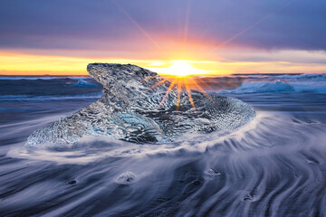 Low angle view at sunrise with a shark shaped iceberg floating on the water in the black sand beach...